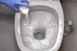 personne versant un mélange de bicarbonate de soude et de vinaigre dans les toilettes